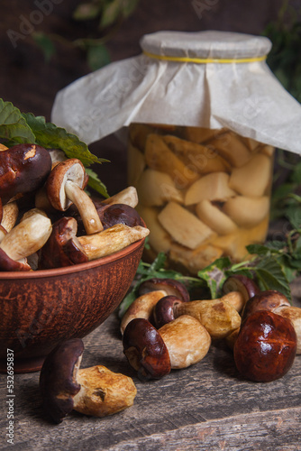 Pile of Imleria Badia or Boletus badius mushrooms commonly known as the bay bolete with canned mushroom in glass jar on vintage wooden background..