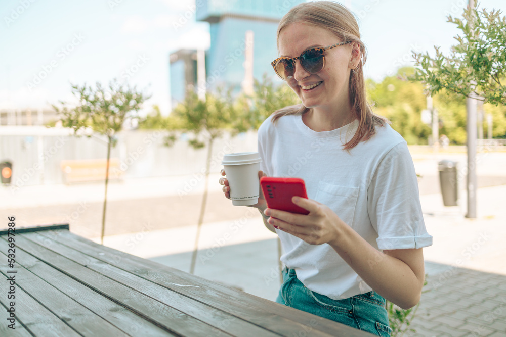 Caucasian young woman holding using smart phone cellphone for e-banking remote work while drinking coffee in street cafe restaurant. 