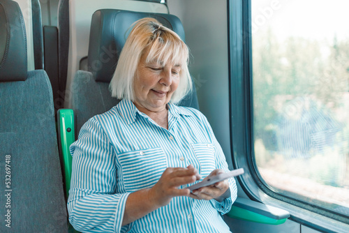 Blonde Caucasian senior woman using transport application on smartphone while travelling by high speed train