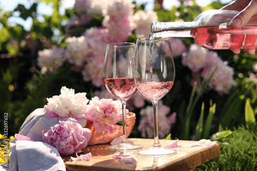 Fototapeta Naklejka Na Ścianę i Meble -  Woman pouring rose wine into glass at table in garden, closeup