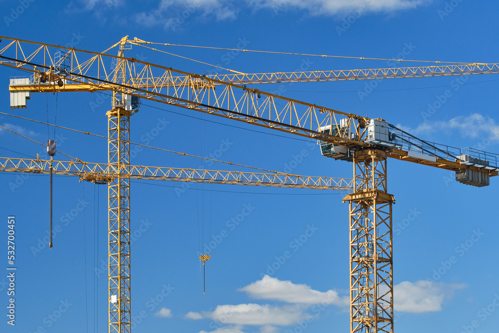 Cranes at construction site. Large construction site, cranes. Tower cranes in action on blue sky background. Housing renovation concept. Selective focus