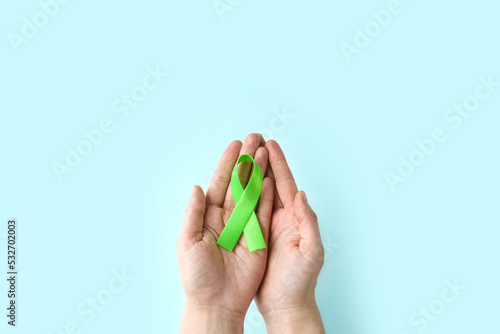 World Mental health awareness day. Woman hands holding green ribbon on blue background. photo