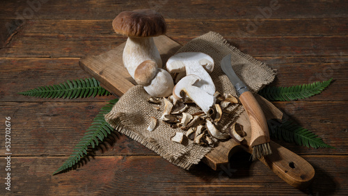 Dark food photography background - Forest mushrooms / Boletus edulis (king bolete) / penny bun / cep / porcini / mushroom, knife and fern on old wooden cutting board on table. photo