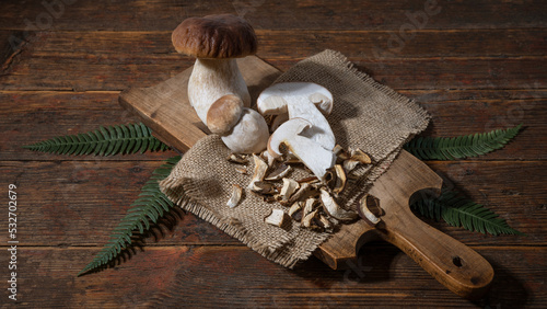 Dark food photography background - Forest mushrooms / Boletus edulis (king bolete) / penny bun / cep / porcini / mushroom and fern on old wooden cutting board on table.. photo