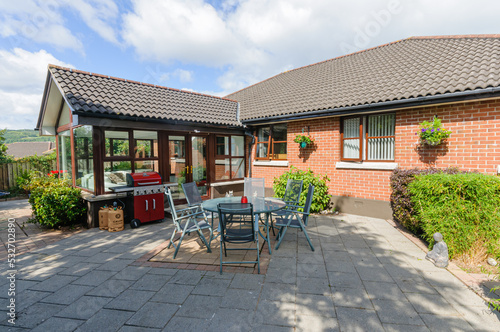 Modern patio with a table, chairs and barbeque behind a bungalow and sunroom. photo