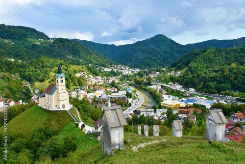 View of the town of Idrija in Primorska, Slovenia and the church of St. Anton and the way of the cross on the slope above with forest covered hills behind the town photo