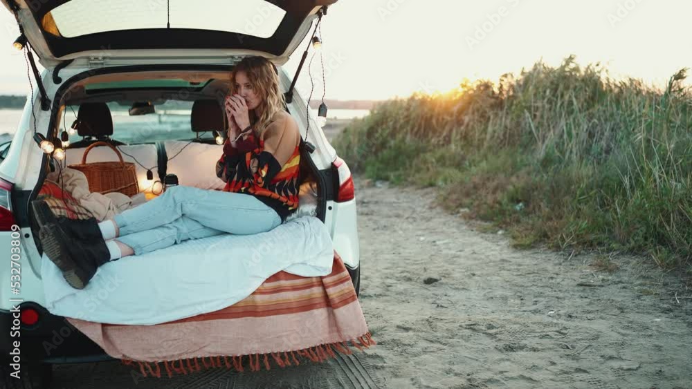 Positive blonde young woman drinking cup of tea in the trunk of the car Positive blonde young woman drinking cup of tea in the trunk of the car