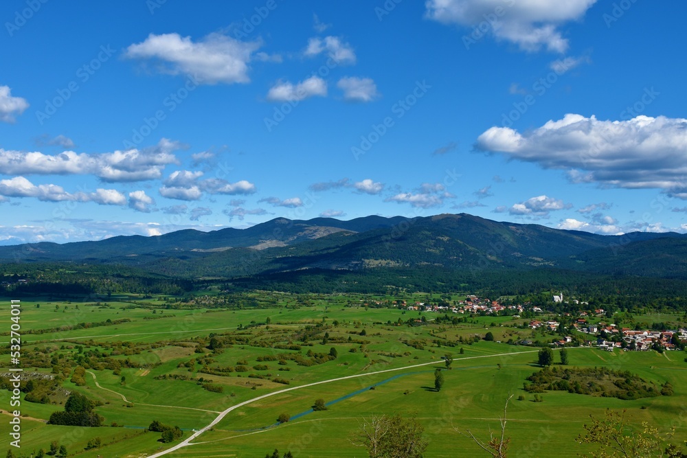View of forest covered Javorniki mountains and green fields and a village bellow in Notranjska, Slovenia