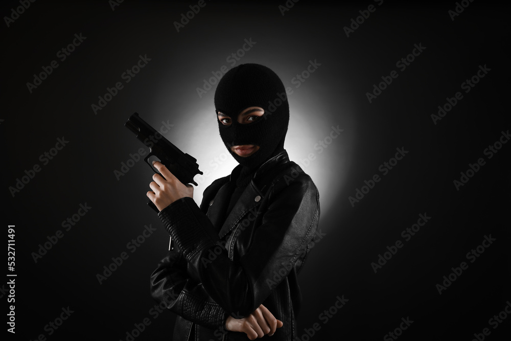 Woman wearing knitted balaclava with gun on black background Woman wearing knitted balaclava with gun on black background
