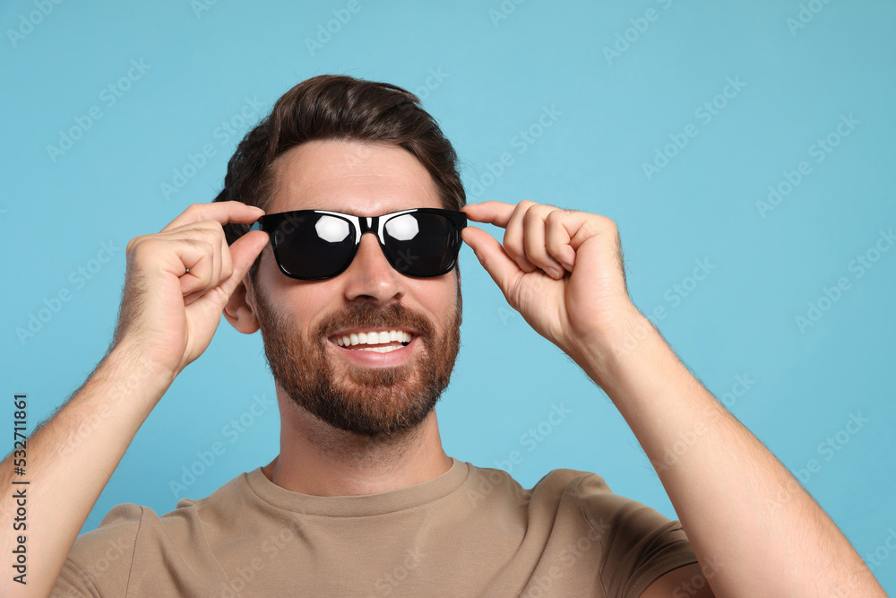 Portrait of smiling bearded man with stylish sunglasses on light blue background, closeup Portrait of smiling bearded man with stylish sunglasses on light blue background, closeup