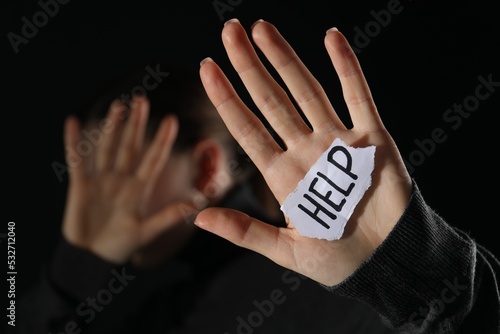 Woman holding piece of paper with word Help on black background, closeup. Domestic violence concept