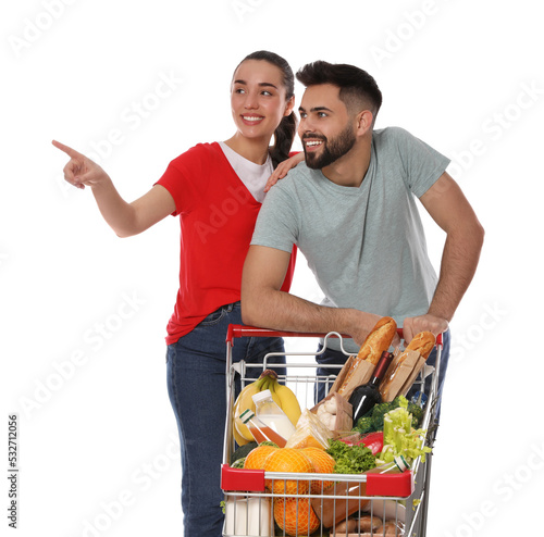 Happy couple with shopping cart full of groceries on white background