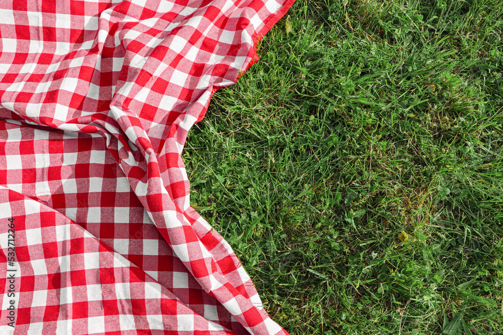 Checkered picnic tablecloth on fresh green grass, top view. Space for text Checkered picnic tablecloth on fresh green grass, top view. Space for text
