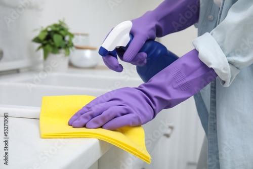 Woman cleaning white countertop with rag and detergent indoors, closeup