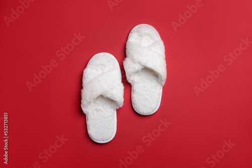 Pair of soft white slippers on red background, top view