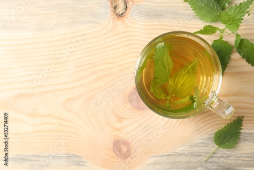 Glass cup of aromatic nettle tea and green leaves on wooden table, flat lay. Space for text