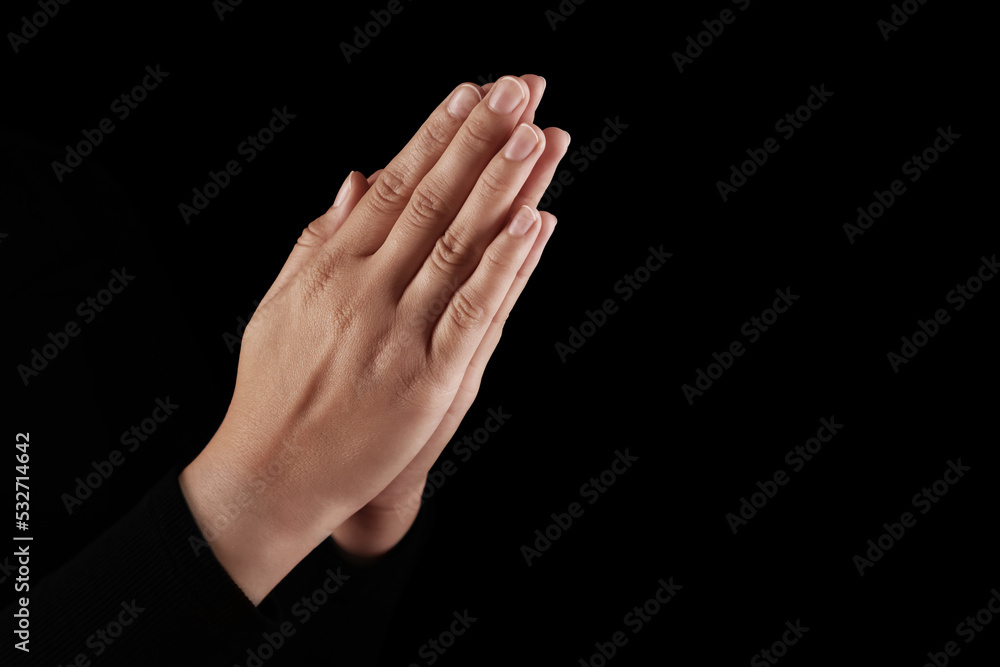 Woman holding hands clasped while praying in darkness, closeup. Space for text