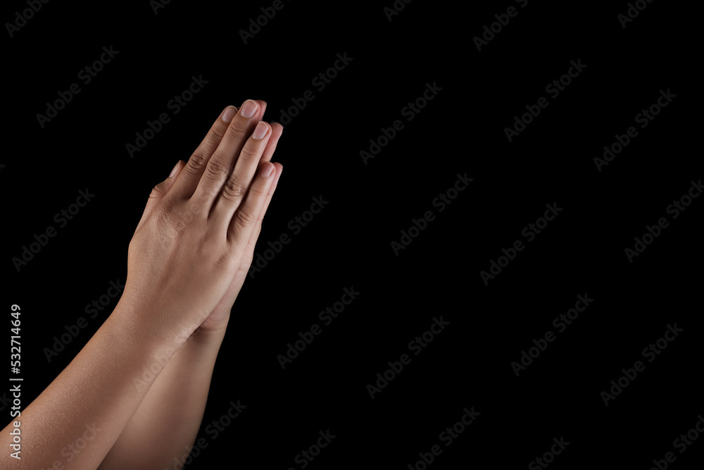 Woman holding hands clasped while praying on black background, closeup. Space for text