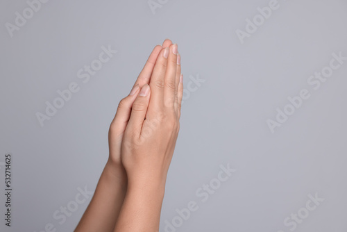 Woman holding hands clasped while praying against light grey background, closeup. Space for text