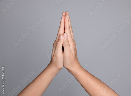 Woman holding hands clasped while praying against light grey background, closeup
