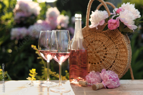 Fototapeta Naklejka Na Ścianę i Meble -  Bottle and glasses of rose wine near beautiful peonies on wooden table in garden