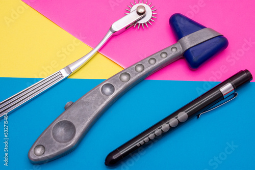 Neurological diagnostic tools: hammer, flashlight for checking pupillary response to light, Wartenberg wheel or neurowheel lie on abstract pink, yellow and blue background. Photo for use in neurology  photo