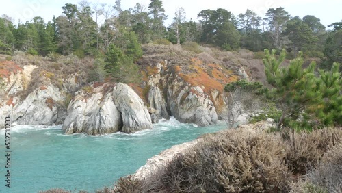 Coniferous pine cypress tree, bare rock, crag or cliff, ocean beach, blue sea water waves in bay. Nature near Big Sur, 17-mile drive. Trail to China Cove, Point Lobos, Monterey, California coast, USA.