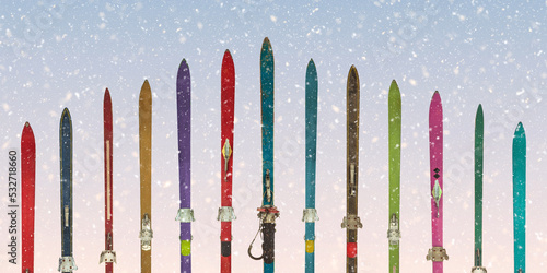 Row of vintage weathered skis in front of a blue sky with snowfall