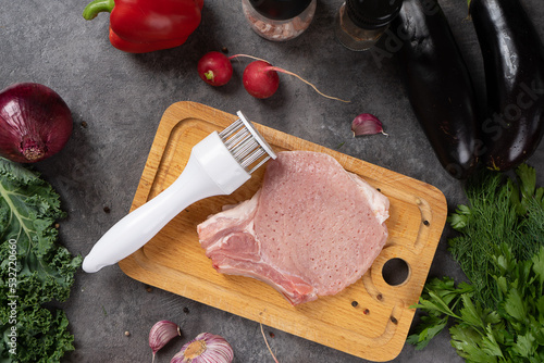 Fresh meat on a wooden cutting board. Next to meat with vegetables and spices and tenderizer for meat.
