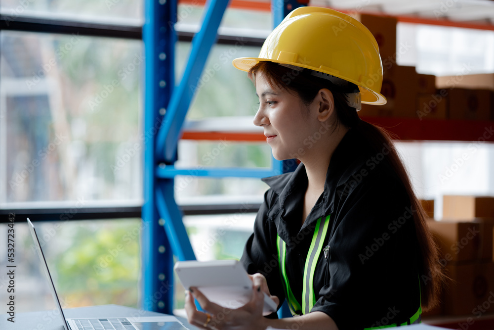 Asian female worker wearing a safety vest is in a warehouse, checking orders and checking balances in a computer system. The concept of working in the warehouse and working in the warehouse is safe. Asian female worker wearing a safety vest is in a warehouse, checking orders and checking balances in a computer system. The concept of working in the warehouse and working in the warehouse is safe.