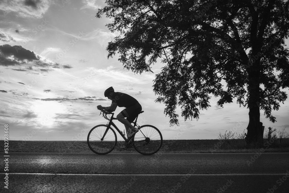 Obraz premium Young sports man cycling with bicycle on the road in summer in black and white