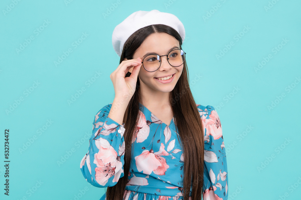Headshot portrait of cute teenager child girl isolated on blue studio background wear glasses look at camera, kid eyesight treatment concept. Happy teenager, positive and smiling emotions.