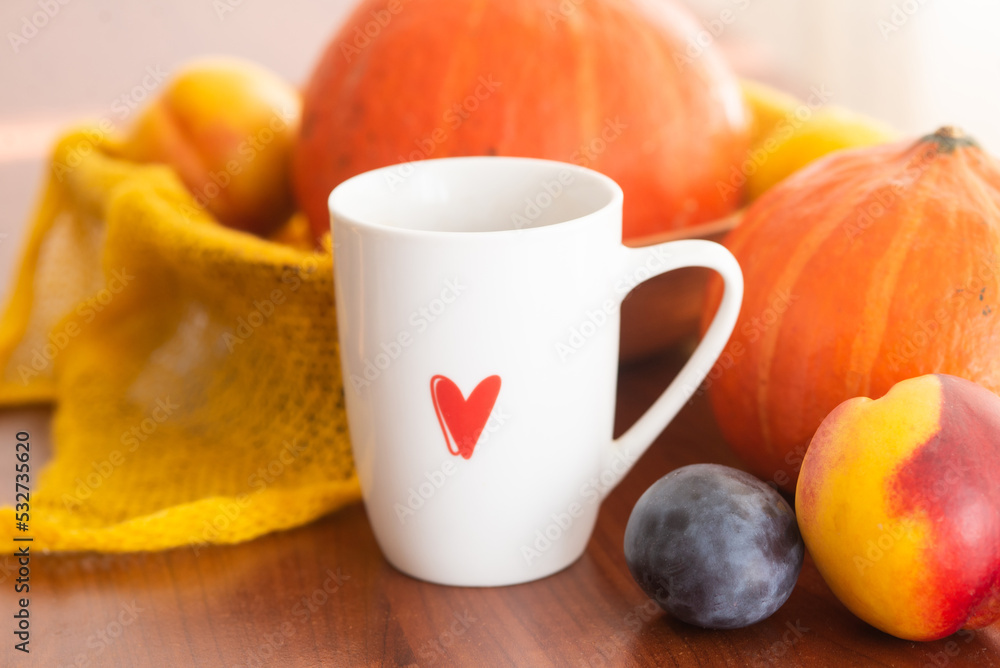 white cup with a red heart pattern of tea with an autumn decor of pumpkins, plums, textiles and peaches on a wooden background white cup with a red heart pattern of tea with an autumn decor of pumpkins, plums, textiles and peaches on a wooden background