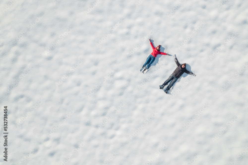 Happy man and woman (couple) lying on the snow at winter, christmas day. Drone, top, aerial view.