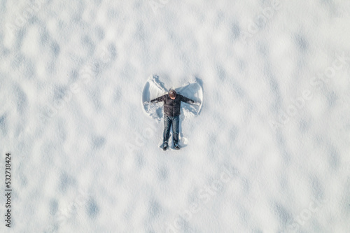 Man lying on a snow and doing angel print on a snow covered land. Aerial, top view. Drone photo. Winter