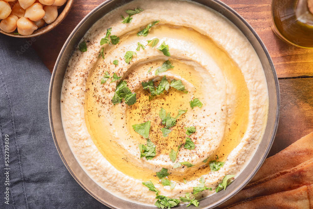Arabic cuisine; Traditional creamy hummus dip in dark bowl. Topped with olive oil, paprika and parsley. Top view with close up. Arabic cuisine; Traditional creamy hummus dip in dark bowl. Topped with olive oil, paprika and parsley. Top view with close up.