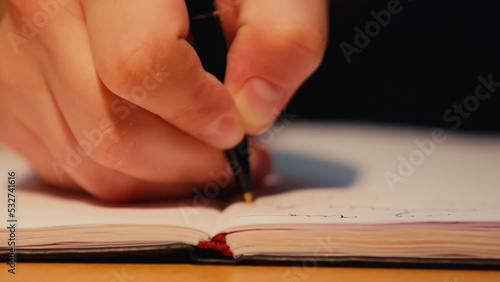 cropped view of man holding pen while writing in notebook on desk.