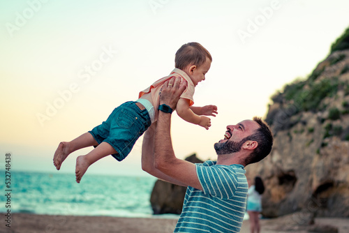 Papá e hijo bebé niño sonriente en la playa jugando y divirtiendose  photo