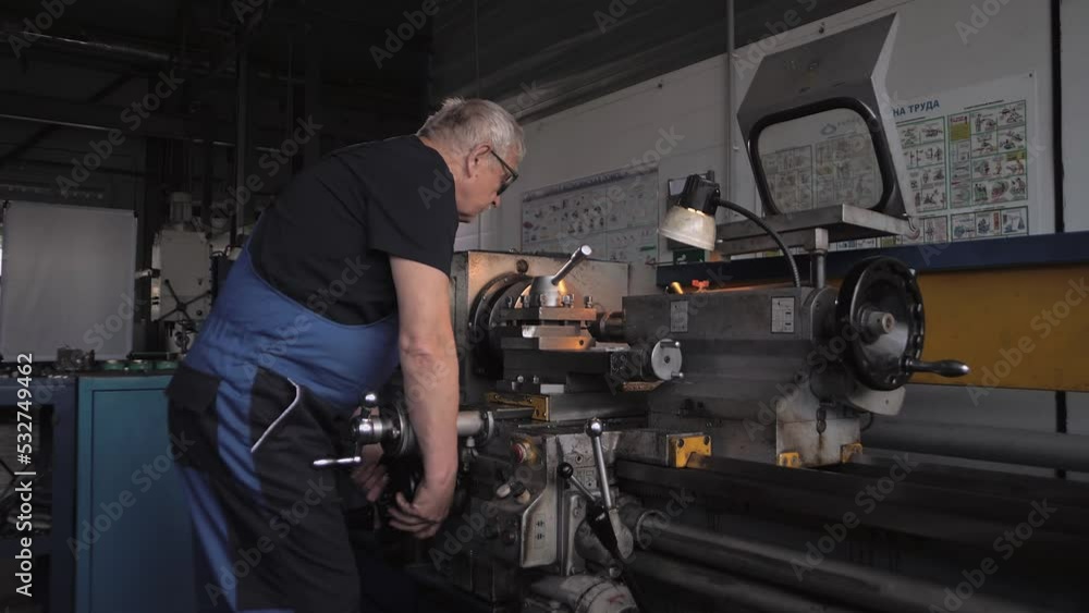 Elderly man in a work uniform works on a huge lathe Elderly man in a work uniform works on a huge lathe