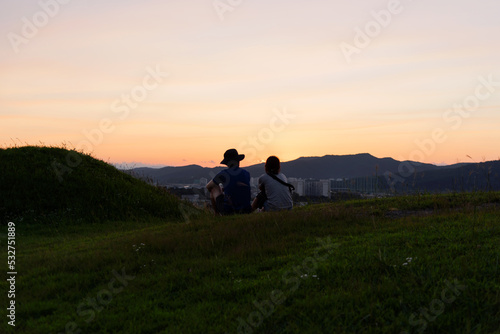 Lovely Couple sitting on the green hill to enjoy sunset