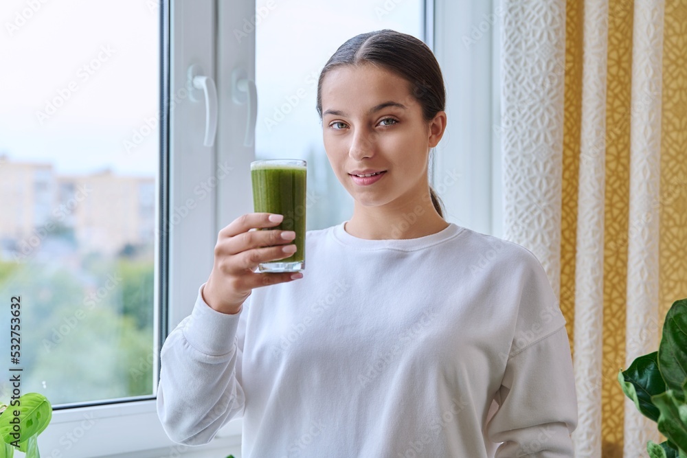 Young teenage female holding glass with fresh green vegetable herbal smoothie Young teenage female holding glass with fresh green vegetable herbal smoothie