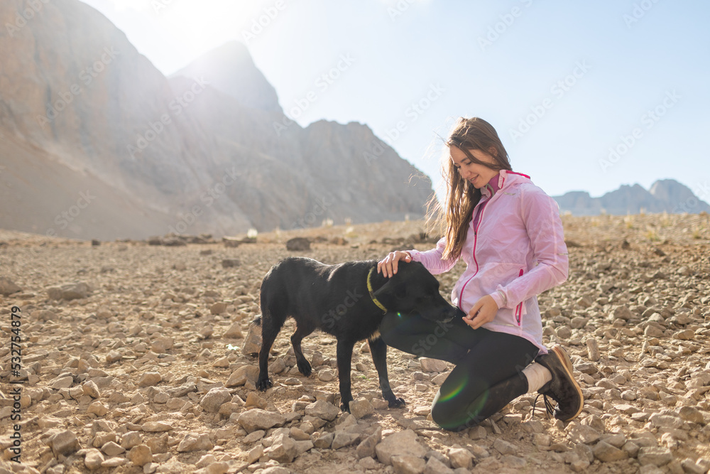 young woman plays with a black dog on a background of mountains. travel and freedom concept young woman plays with a black dog on a background of mountains. travel and freedom concept