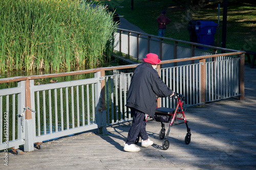 Photography A senior female walking in the public park with a wheeled walker
