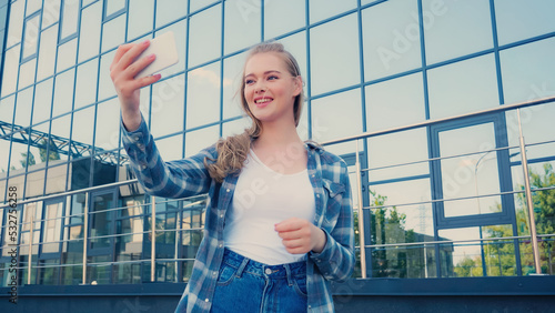 Blonde woman taking selfie on smartphone on urban street.