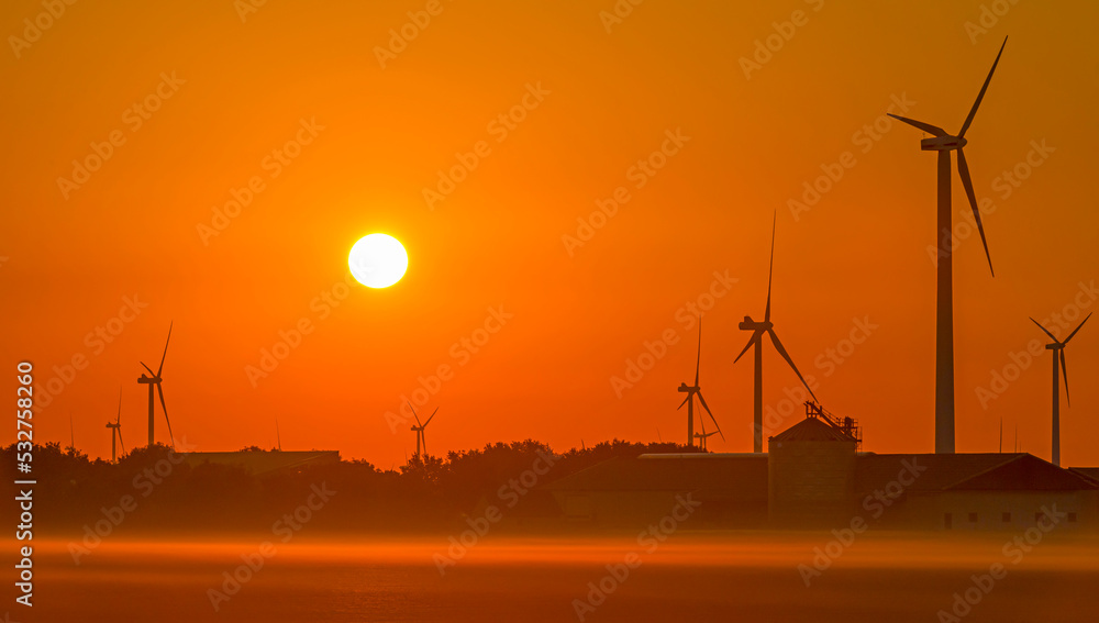 Fototapeta premium Wind turbines in a foggy agricultural field in sunlight at sunrise in autumn, Almere, Flevoland, Netherlands, September, 2022