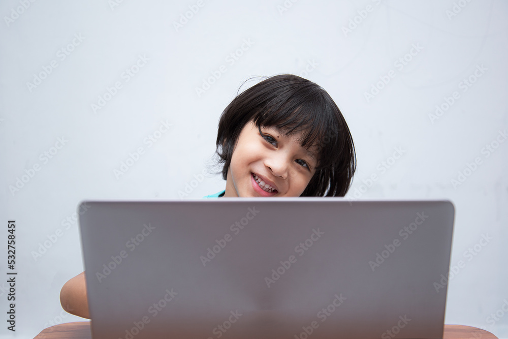 Cute smart Asian boy is happily using his laptop to study online by himself at home. Online learning concept.Self-Study. Cute smart Asian boy is happily using his laptop to study online by himself at home. Online learning concept.Self-Study.