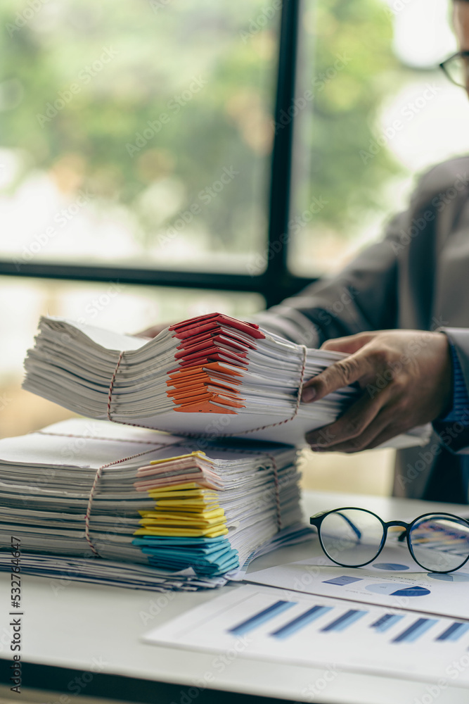 Businessman working in finance with pile of unfinished papers on the desk business paper pile Businessman working in finance with pile of unfinished papers on the desk business paper pile