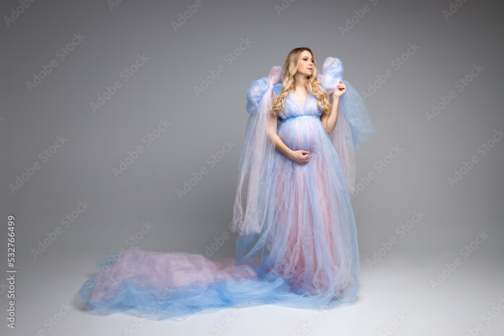 Pregnant girl with blonde hair on a gray background. Dresses for pregnant women. Maternity clothes. Banner with a pregnant girl. Angel in blue dress. Copy space. Space for text.