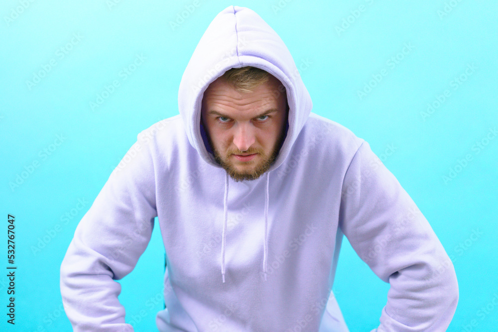 Portrait of a looking under his brows, wearing a purple hoodie on a blue background. Rebel. Threatening. Fashion. Anger. Dude. Beard. Lifestyle. Spite. Confident. Emotion. Confidence. Photogenic. Scar Portrait of a looking under his brows, wearing a purple hoodie on a blue background. Rebel. Threatening. Fashion. Anger. Dude. Beard. Lifestyle. Spite. Confident. Emotion. Confidence. Photogenic. Scar