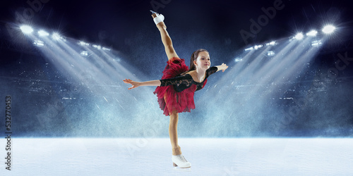 Beautiful female beginner figure skater in stage dress skating at ice arena with spotlights. Dance, winter sports, achievements, champion concept